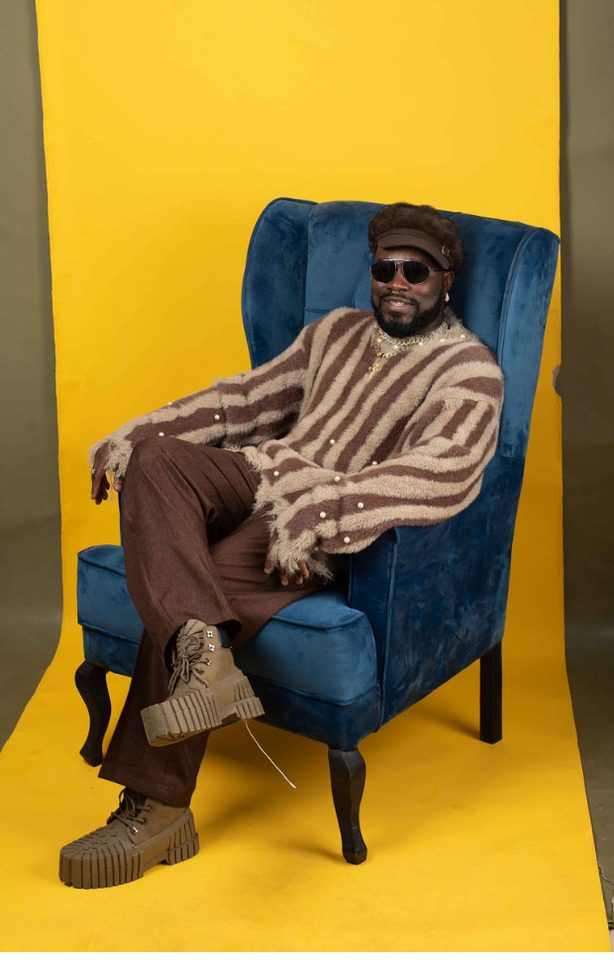 Don Crucifixto seated in a blue wing chair against a yellow backdrop